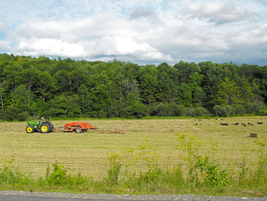 A John Deere tractor pulling a square baler and bale sledge through a Vermont hay field, with finished small square bales lying in the stubble