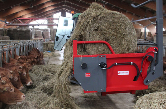 Three-point mounted round bale unroller peeling a net-wrapped round bale into sheets in a field