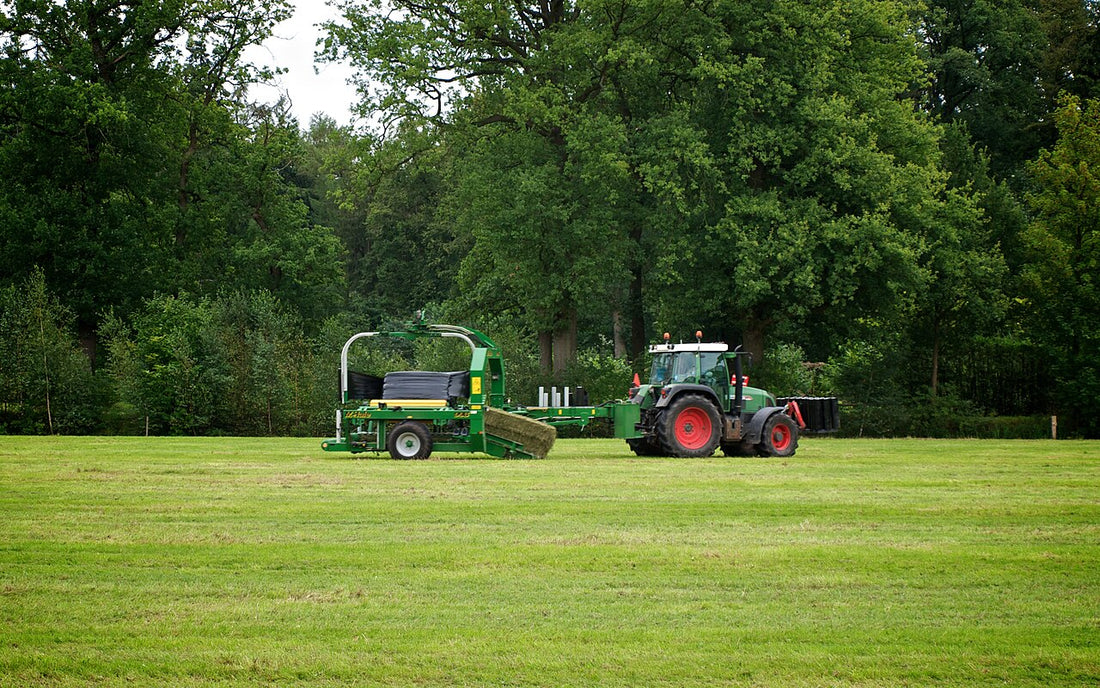Fendt tractor towing a green McHale 998 square bale wrapper picking up a square hay bale and wrapping it in black stretch film in a mown field