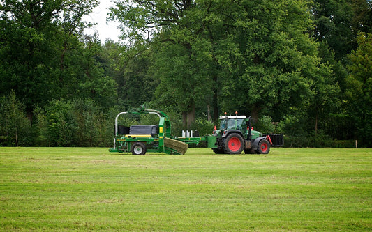Fendt tractor towing a green McHale 998 square bale wrapper picking up a square hay bale and wrapping it in black stretch film in a mown field