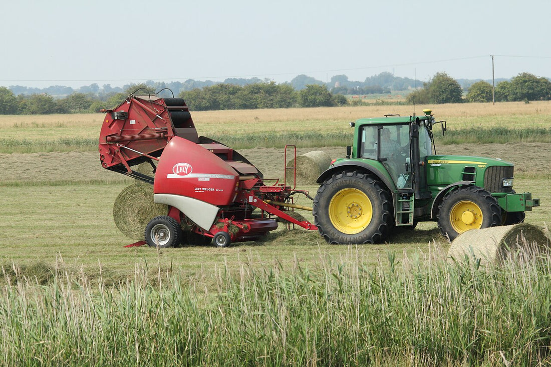 A John Deere 6930P tractor running a Lely Welger RP 435 round baler in a field of round hay bales