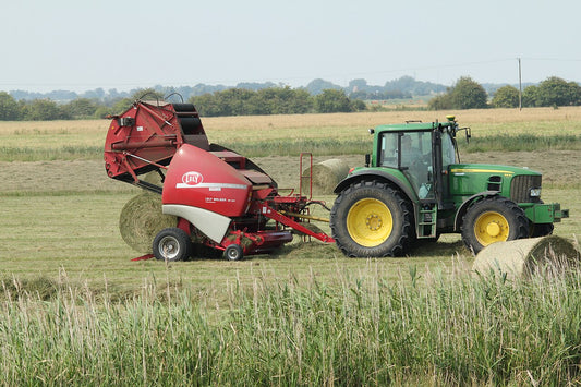 A John Deere 6930P tractor running a Lely Welger RP 435 round baler in a field of round hay bales