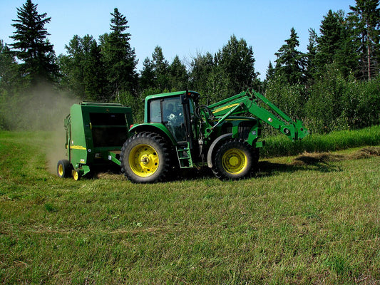John Deere 7420 tractor pulling a John Deere 567 MegaWide round baler through a mown hayfield, dust rising from the pickup