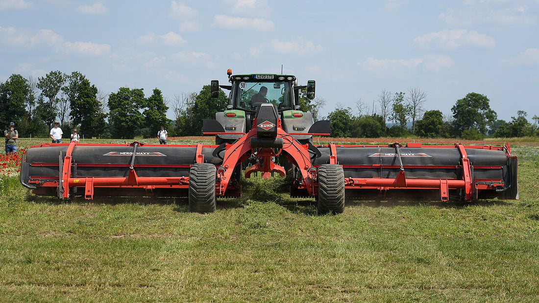 A Kuhn Merge Maxx 1090 twin-belt hay merger working behind a tractor, lifting two swaths onto its conveyor belts and laying them down as one clean windrow