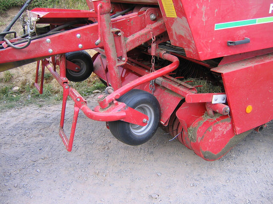 Close-up of the front of a round baler showing the hitch, drawbar, gauge wheels, and pickup where the PTO driveline and slip clutch mount