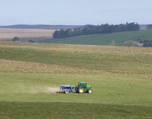 Tractor pulling a spreader applying fertilizer across a green grass hay field