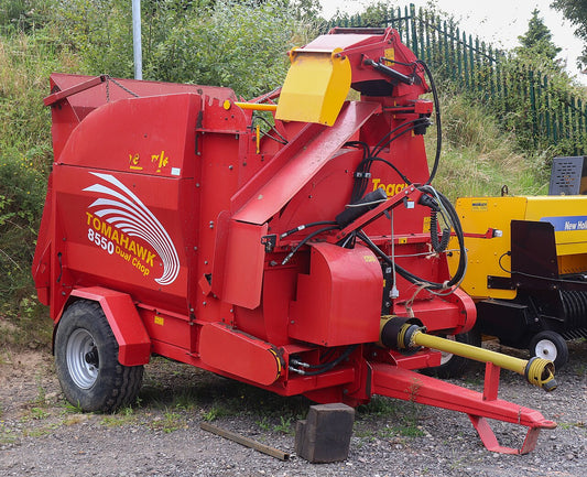 Red trailed bale processor with PTO shaft, feed hopper and swivelling discharge chute, parked in a dealer yard