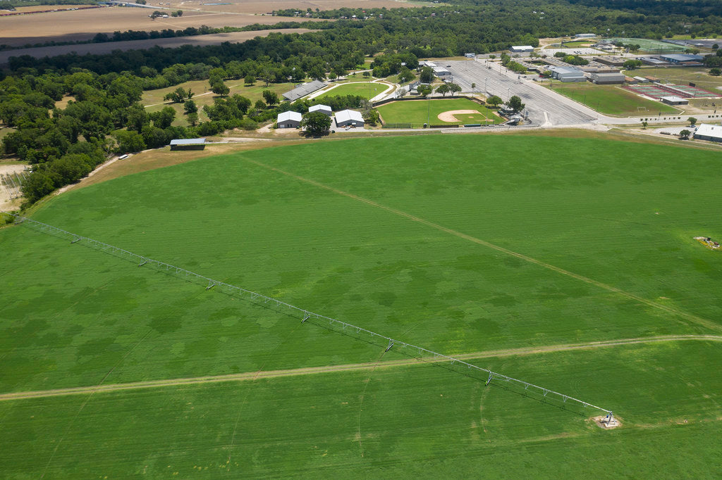 Aerial view of a center-pivot irrigation system crossing a green hayfield at Schirmer Farms in Texas.