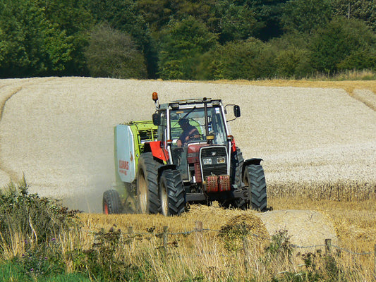 A Claas round baler at work behind a tractor in a stubble field, making large round bales