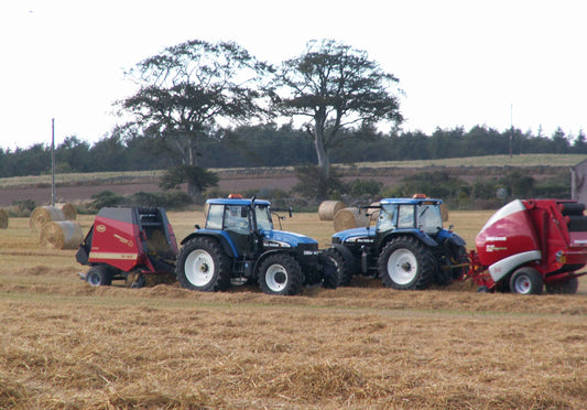 Two tractors attached to round balers in a harvested field in Scotland.