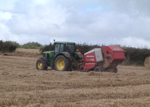 Green tractor pulling a red round baler through light straw windrows in a harvested wheat field