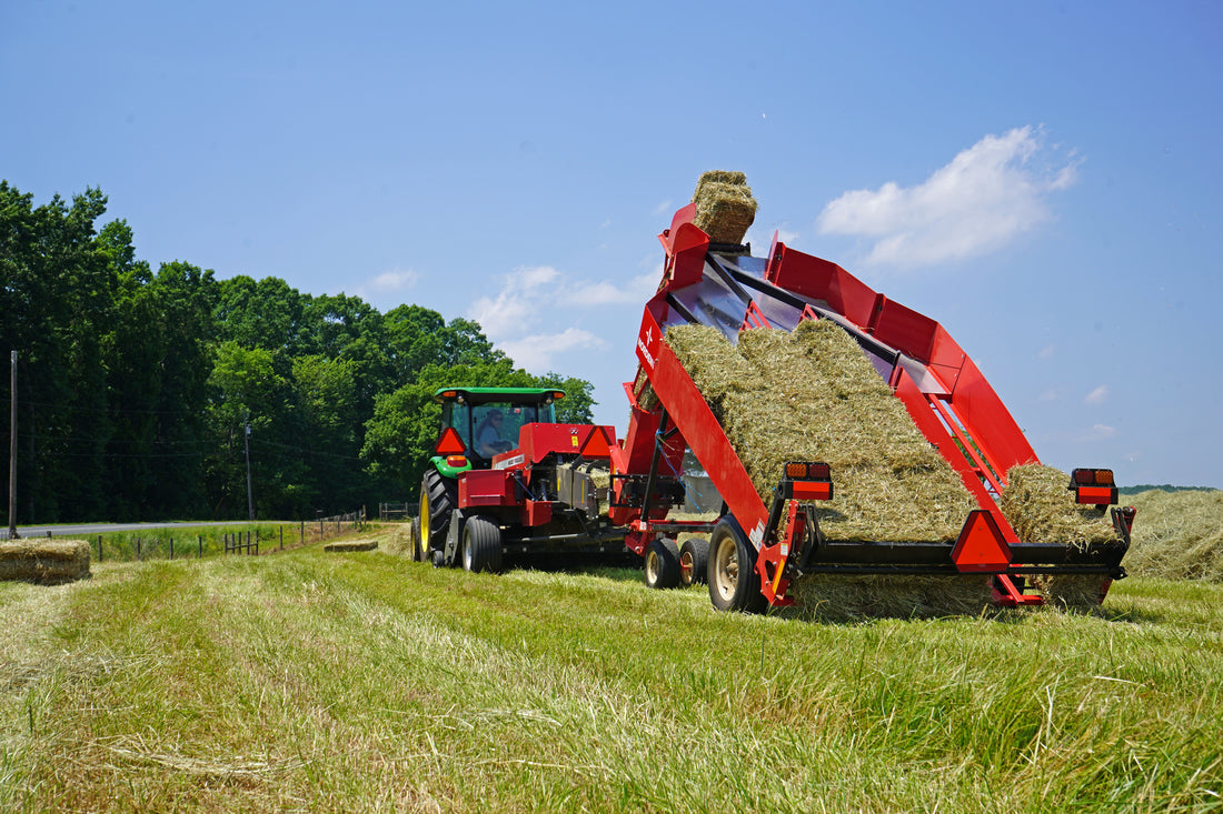 John Deere tractor pulling a small square baler and a red bale accumulator dropping small square hay bales in a green field