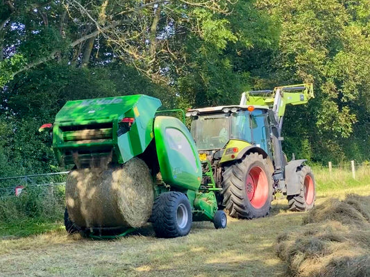 A McHale round baler ejecting a net-wrapped round bale with the tailgate raised in a hayfield