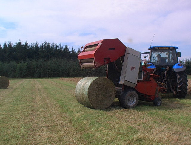 A tractor and round baler baling in a field, the net wrap system working at the tailgate where duckbill and actuator no-start faults occur