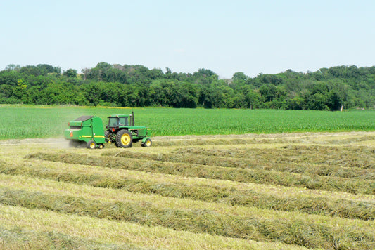 John Deere tractor and round baler working windrows in an Iowa hay field