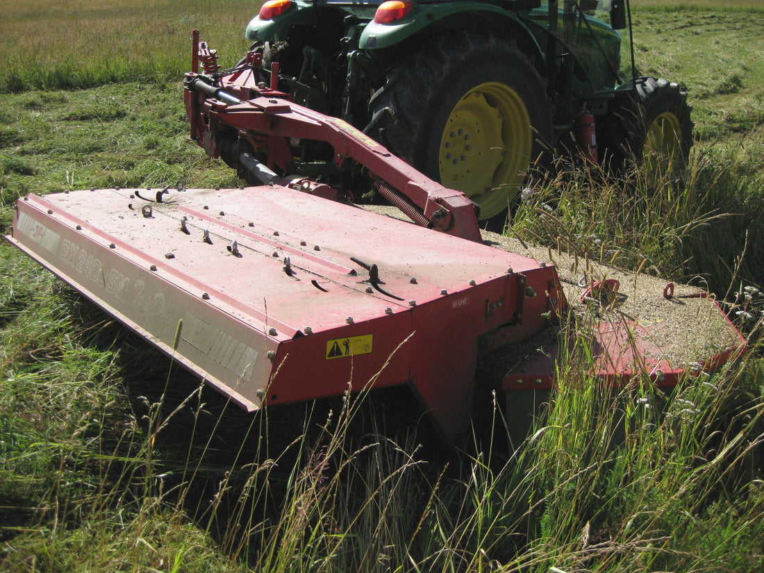A red trailed mower-conditioner pulled by a green tractor cutting a hayfield