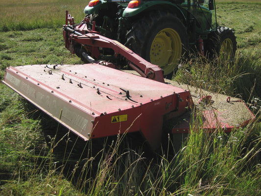 A red trailed mower-conditioner pulled by a green tractor cutting a hayfield