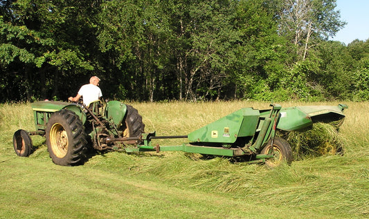 A John Deere tractor pulling a John Deere 1207 sickle-bar mower conditioner, laying a windrow of cut grass hay