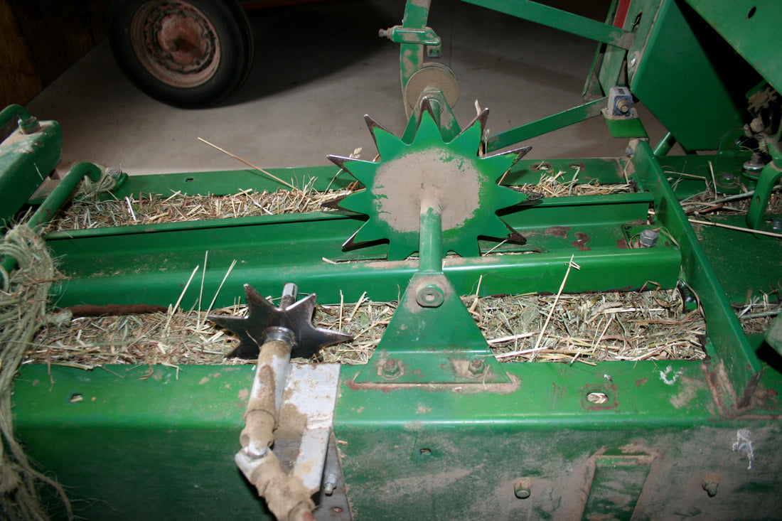 Bale chamber of a John Deere 338 small square baler showing the star-shaped bale length measuring wheel, twine grooves and loose hay