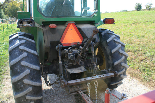 Rear view of a John Deere utility tractor showing the swinging drawbar with multiple hitch holes, three-point hitch lower links and safety chains, with an implement tongue in the foreground