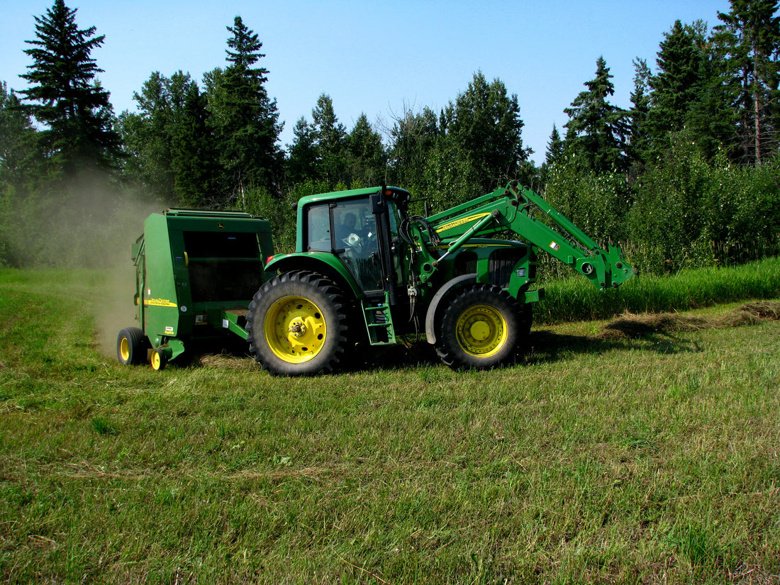 Tractor pulling a John Deere 567 round baler through a dry hay field, the model class where twine arm and half-wrapped bale complaints are most commonly reported