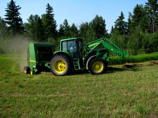 Tractor pulling a John Deere 567 round baler through a dry hay field, the model class where twine arm and half-wrapped bale complaints are most commonly reported