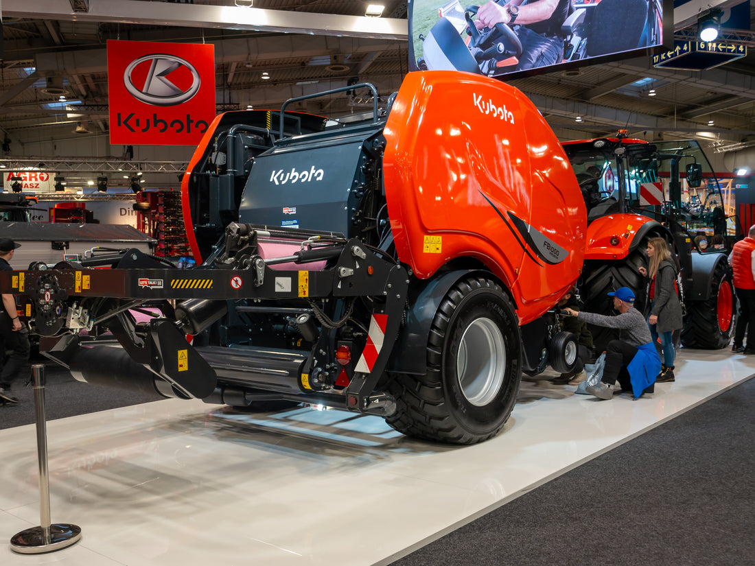 Orange Kubota round baler on display at the Agritechnica farm machinery show in Hanover, with the Kubota logo on the bale chamber cover and pickup