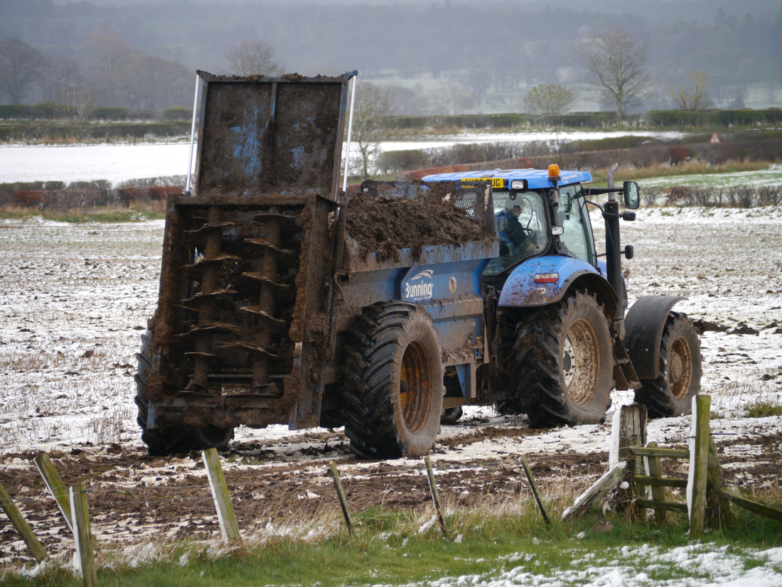 Tractor pulling a rear-discharge manure spreader loaded with solid manure across a field