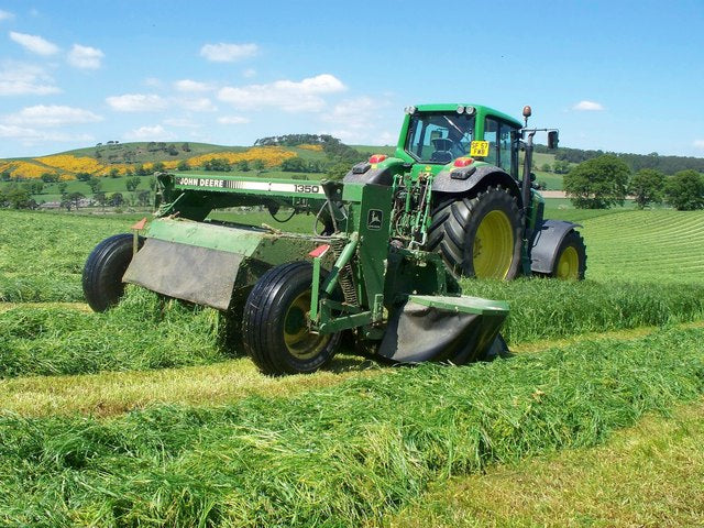 Tractor pulling a mower-conditioner through a grass field, laying the cut crop into a swath behind the machine