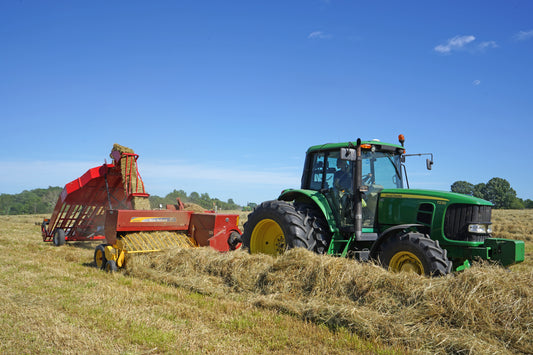 Tractor pulling a small square baler with a bale accumulator mounted behind it, collecting bales into groups in a hay field