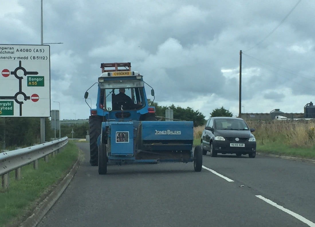 A tractor towing a baler along a public highway with traffic passing, illustrating roading farm equipment