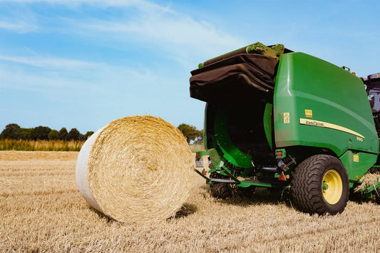 John Deere CoverEdge alternative — green John Deere round baler discharging a bale wrapped in XES Extreme edge-to-edge net wrap