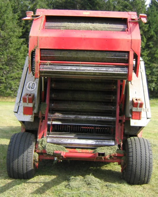 A round baler working in a field — clover is baled before it gets stemmy and wrapped wet as baleage.