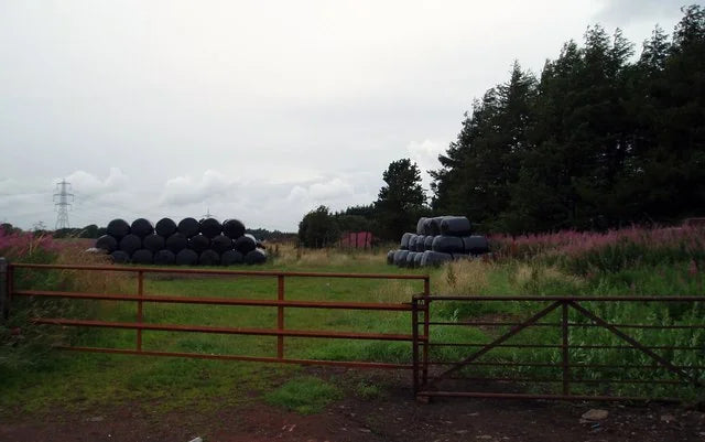 Two stacks of round bales wrapped and held in farm inventory -- the kind of season-long output where net wrap either earns its cost back or it does not.